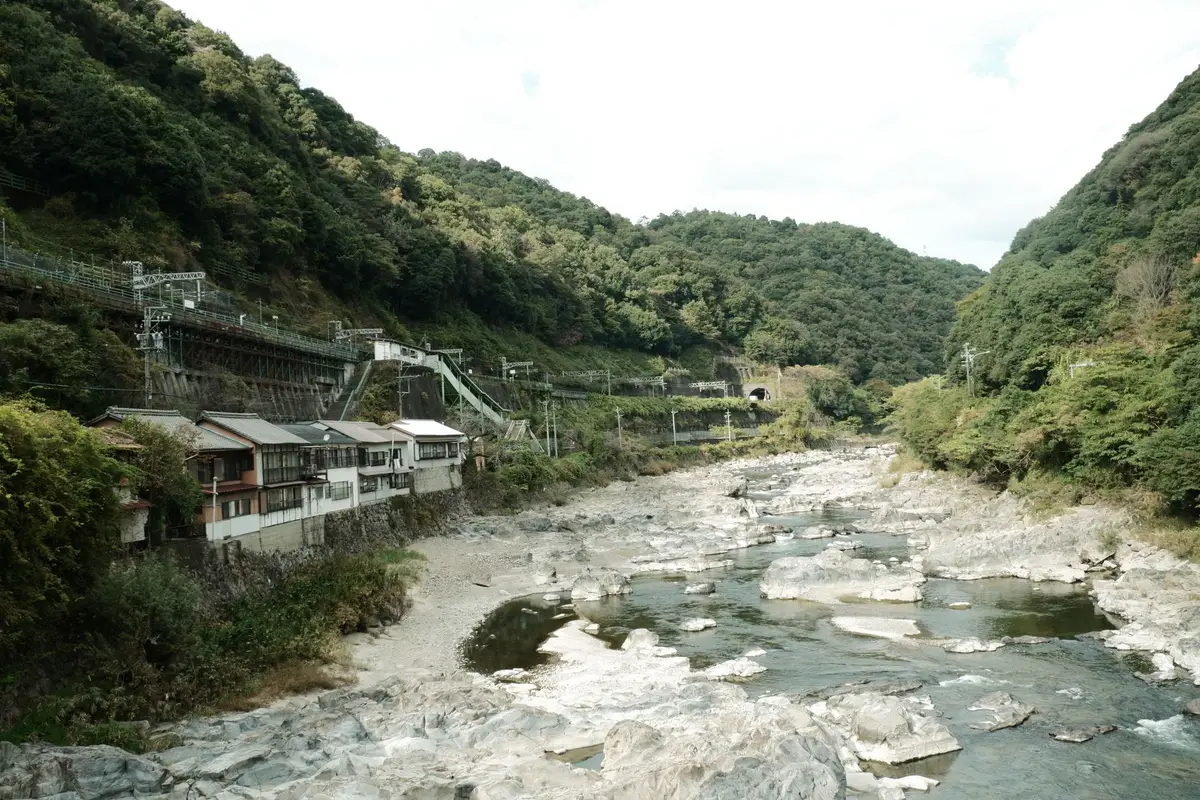 A river valley in rural Japan with houses and a railway along forested hills